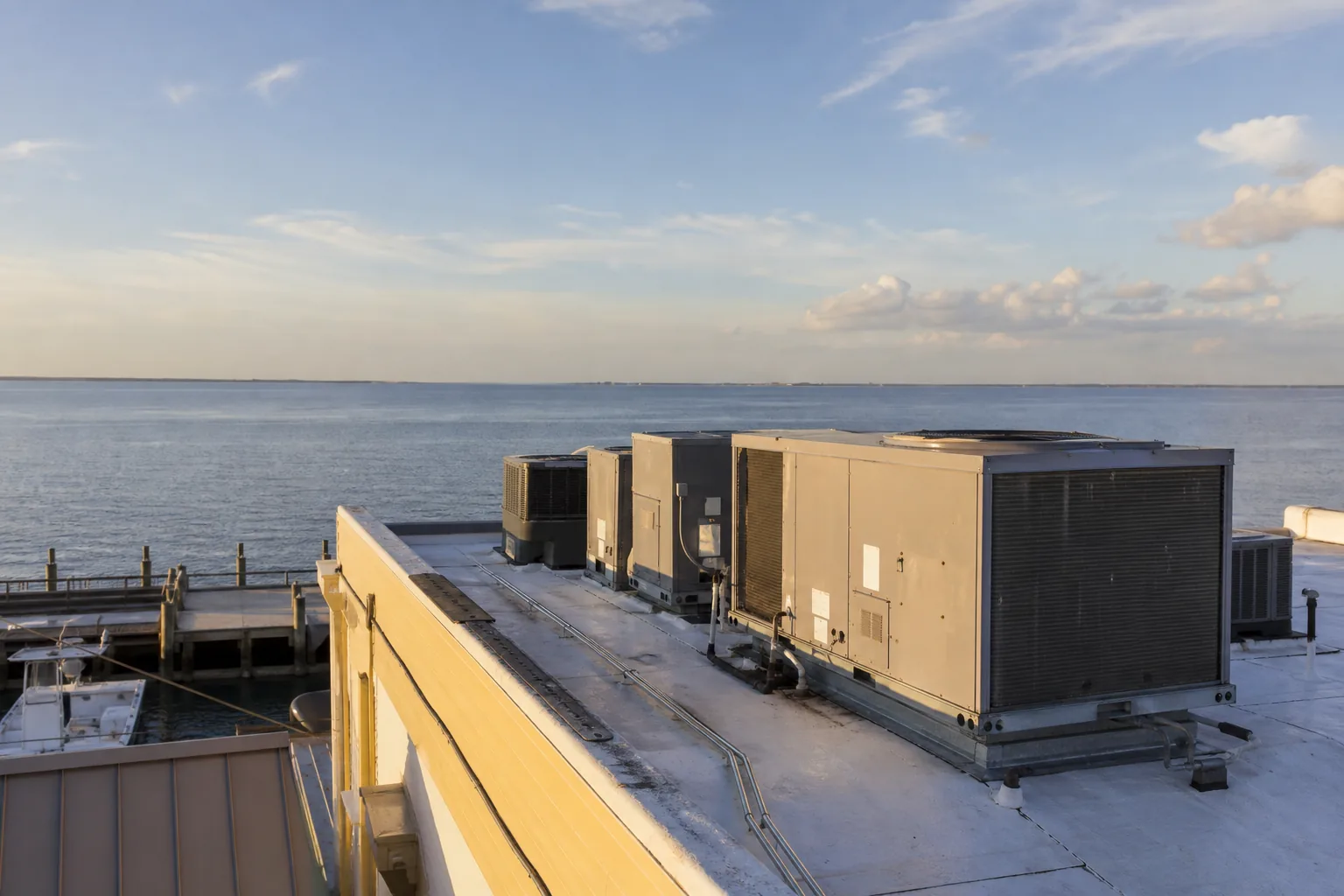 Commercial rooftop HVAC units on a waterfront restaurant building with calm Mobile Bay water and open sky behind in golden afternoon light.